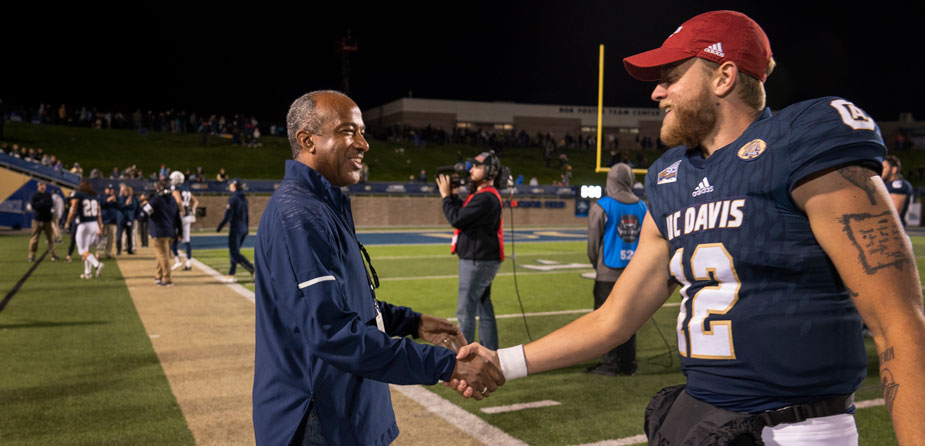 Chancellor May shakes hand of football player on sidelines.