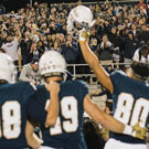 Football player holds up helmet, saluating the fans in the stadium.