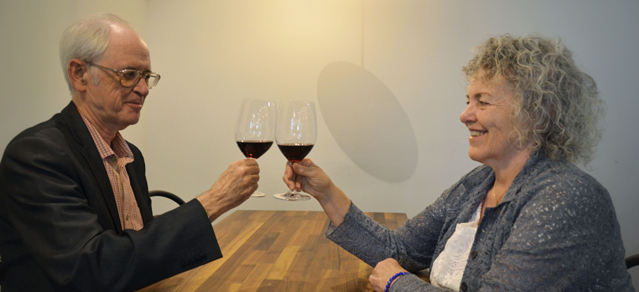 Two people toast across table, each holding a glass of wine.