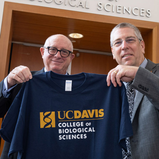 Two men holding College of Biological Sciences T-shirt.