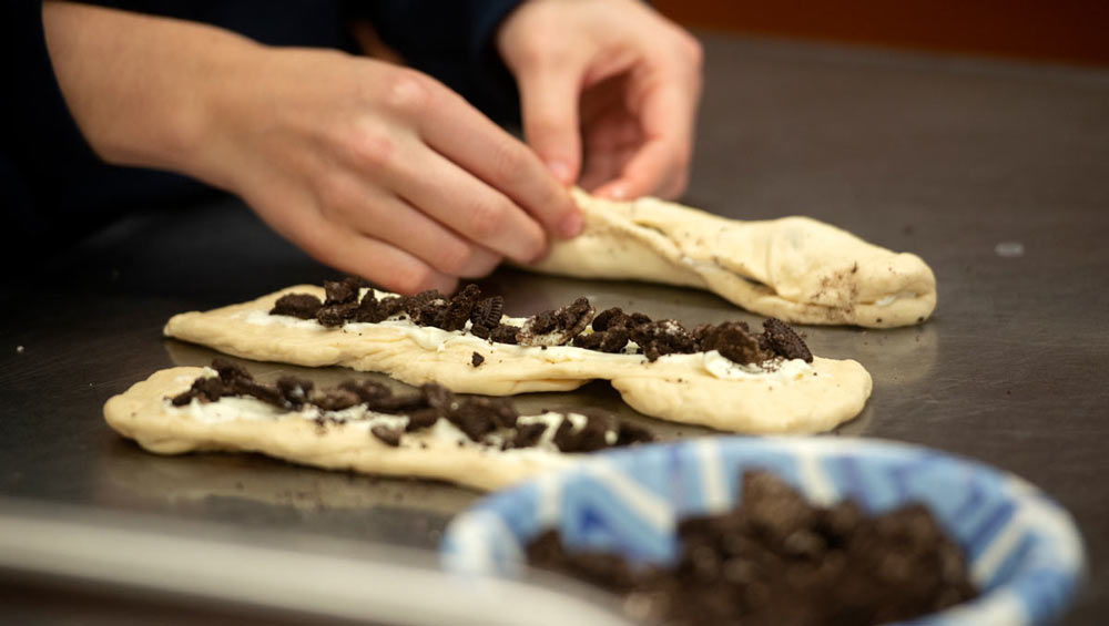 Hands add pieces of Oreo cookies to challah dough.