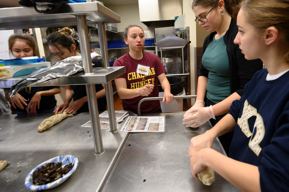 Female student gives instructions to other student volunteers in kitchen.