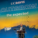 Chancellor Gary S. May stands on stage in front of banner reading "Outgrow the Expected"
