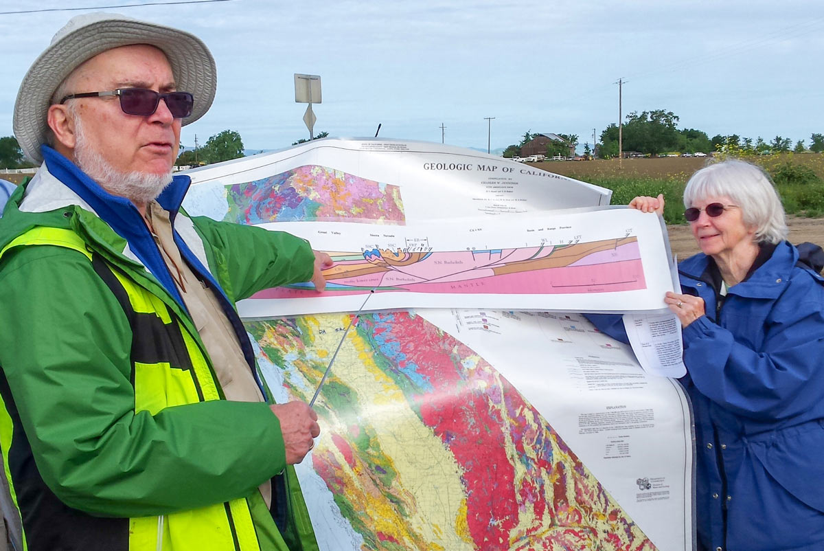 Man and woman flank a map that they are displaying as part of a geology tour.