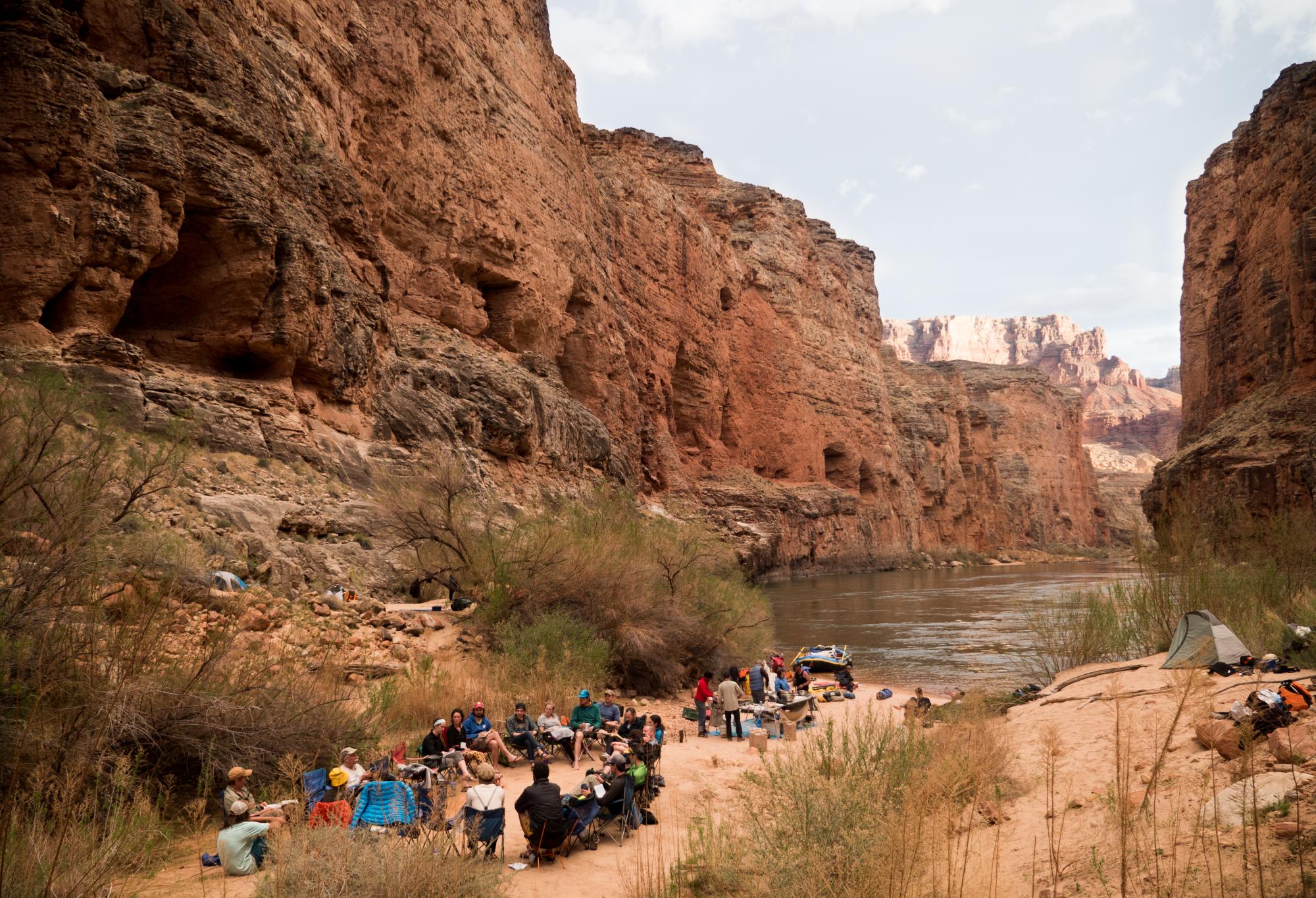 Men and women sit in circle on beach by Colorado River in Grand Canyon