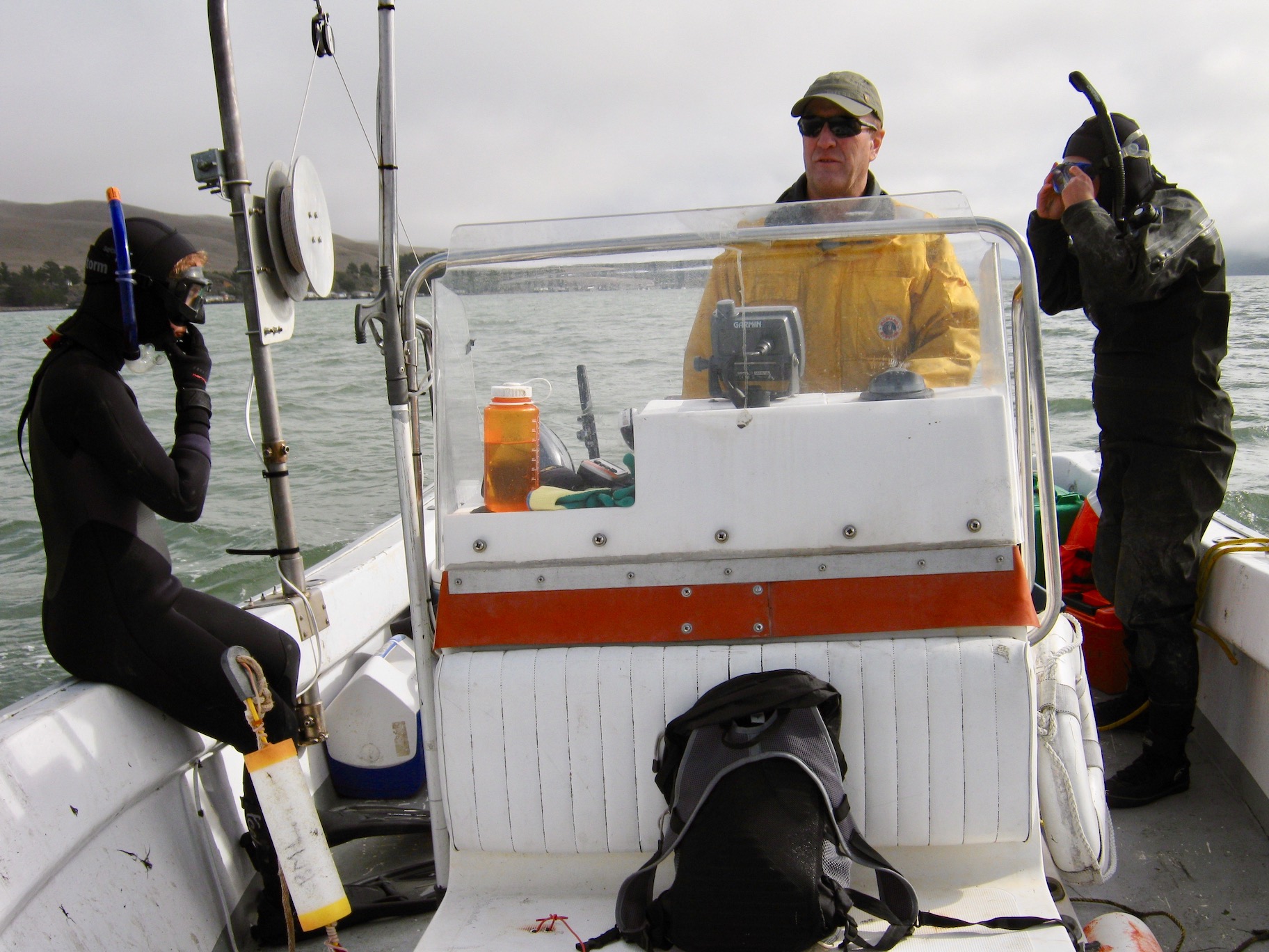 Male scientist drives boat with two SCUBA divers in Tomales Bay
