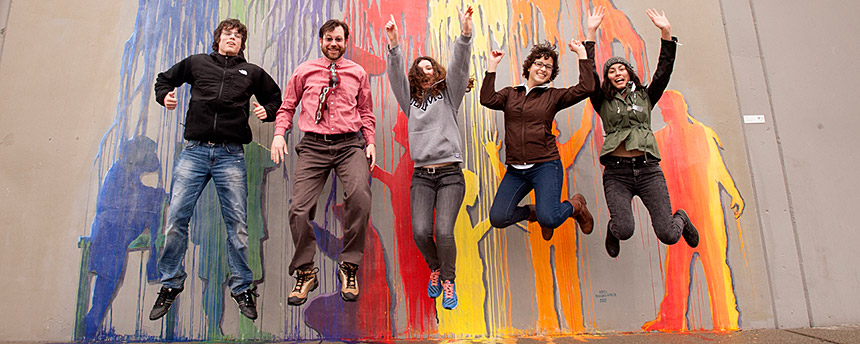 A group of students jumping high with a mural of paint dribbles behind them