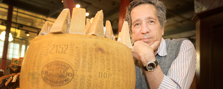 Man looking at the camera behind a big block of parmesan cheese.