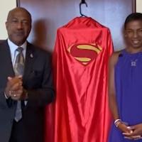 Chancellor Gary May and LeShelle in their home standing in front of a superman costume cape