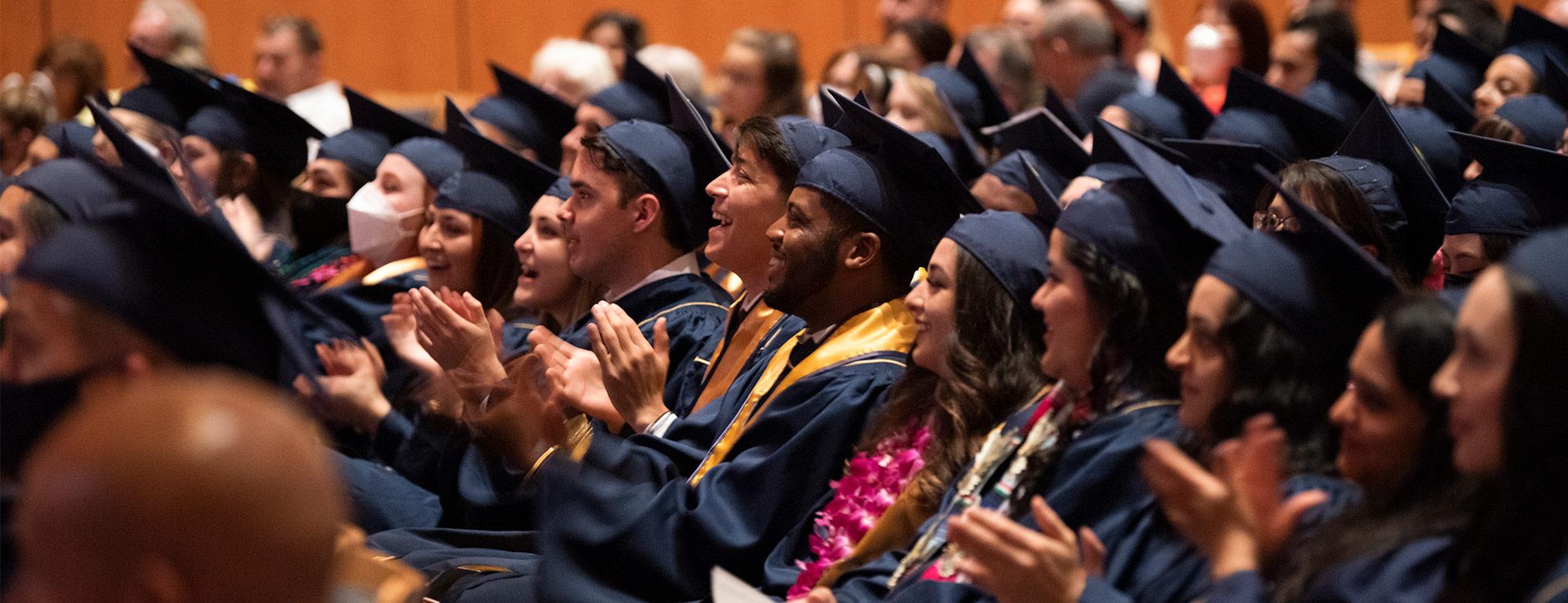 clapping and smiling students in caps and gowns in the Mondavi Center auditorium for a commencement ceremony