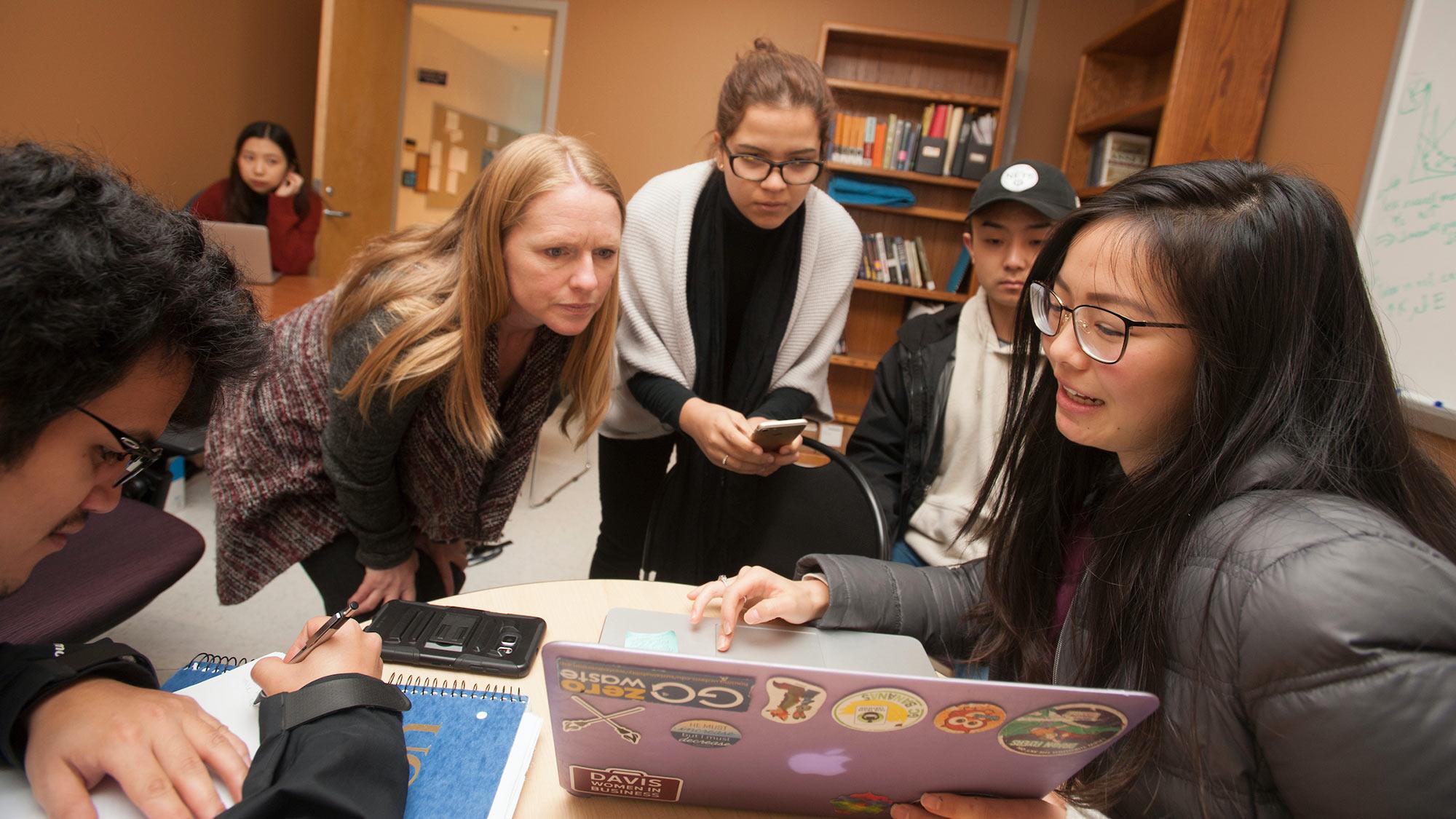 A group of students and their professor gather around a laptop 