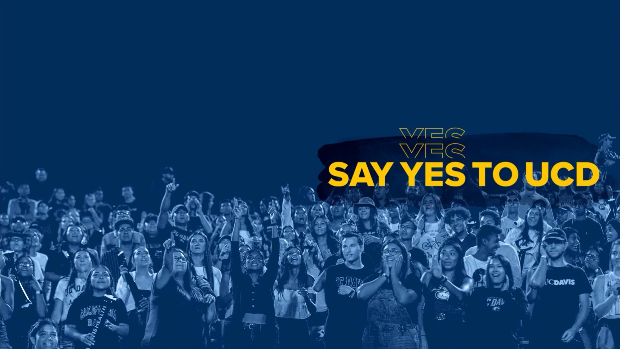 A blue tone image of a large group of students cheering with "Say Yes! to UC Davis over it and confetti raining down