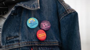 Three multi-colored Eggheads anniversary pins decorate a dark blue denim jacket.