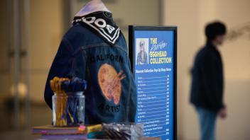 A mannequin wearing a denim jacket emblazoned with “California Artist” and a Bookhead silk scarf is displayed at the Manetti Shrem Museum Collection Pop-Up Shop.