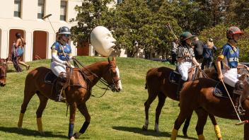 The UC Davis equestrian team rides their horses in front of Mrak Hall and the See No Evil/Hear No Evil Eggheads.