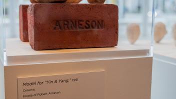 The original Yin & Yang models, showing the Eggheads sitting on top of a brick emblazoned with “Arneson”, sit inside a glass display case in the Manetti Shrem Museum.