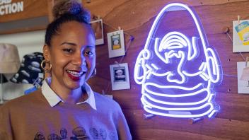 A woman wearing a UC Davis Eggheads sweater stands next to a blue neon Fatal Laff sign at the Year of the Eggheads VIP celebration.