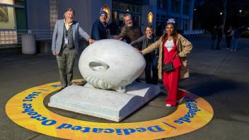 Five Strategic Communications staff members smile happily at the camera while placing their hands on Bookhead at the Year of the Eggheads VIP celebration.