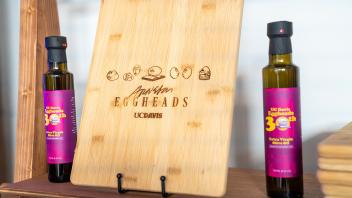 A cutting board with the Eggheads woodburned onto it sits between by UC Davis Eggheads 30th Anniversary olive oil at the Year of the Eggheads VIP celebration.