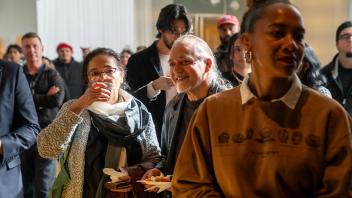 Two people stand together eating and drinking amongst a crowd at the Year of the Eggheads VIP celebration.