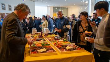 A group of people get and eat appetizers from a table of food at the Year of the Eggheads VIP celebration.