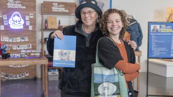 Two women smile happily at the camera and show off their purchases from the Manetti Shrem Museum Collection Pop-Up Shop.