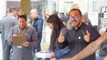 A Strategic Communications staff member smiles at the camera and gives two thumbs up at the Year of the Eggheads VIP event check-in.