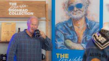 Robert Arneson’s son, Kirk Anderson, stands in front of the Arneson Egghead Collection display and pretends to drink out of a mug emblazoned “Arneson”.