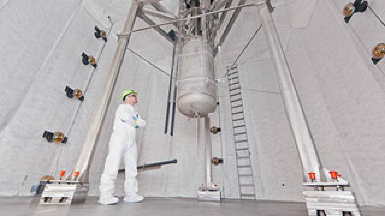 Man in white suit in a huge tank looking at a hanging dark matter detector