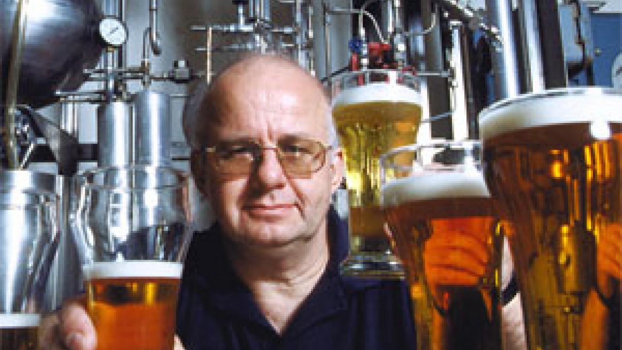 Photo: man posing with several glasses of beer with brewing facilities in background
