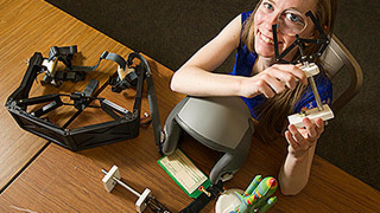 Woman staring through an optical device looking up at the camera, with various devices on the table