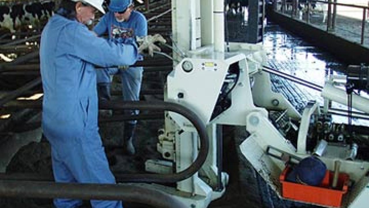 Photo: Two researchers in suits and hard hats work on drilling machine in dairy.