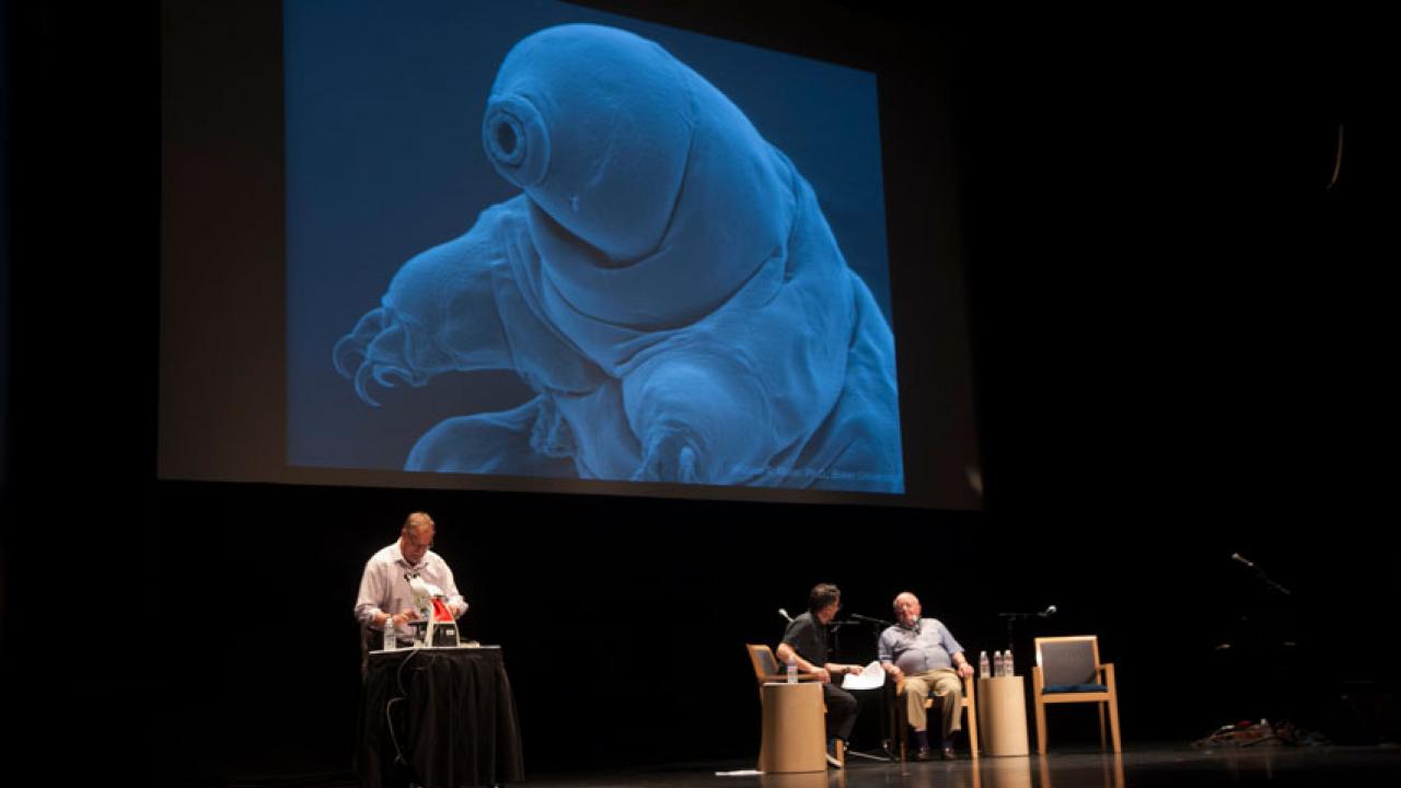 &ldquo;Science Friday&rdquo; host Iraw Flatow and Professor Emeritus John Crowe, on stage, with picture of a tartigrade (enlarged) on screen