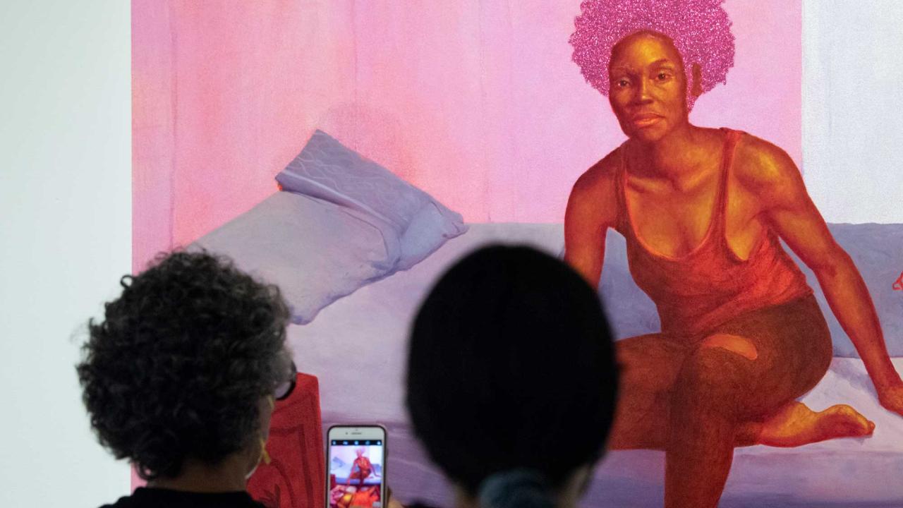 Museum patrons in foreground look at art portrait of woman with pink hues