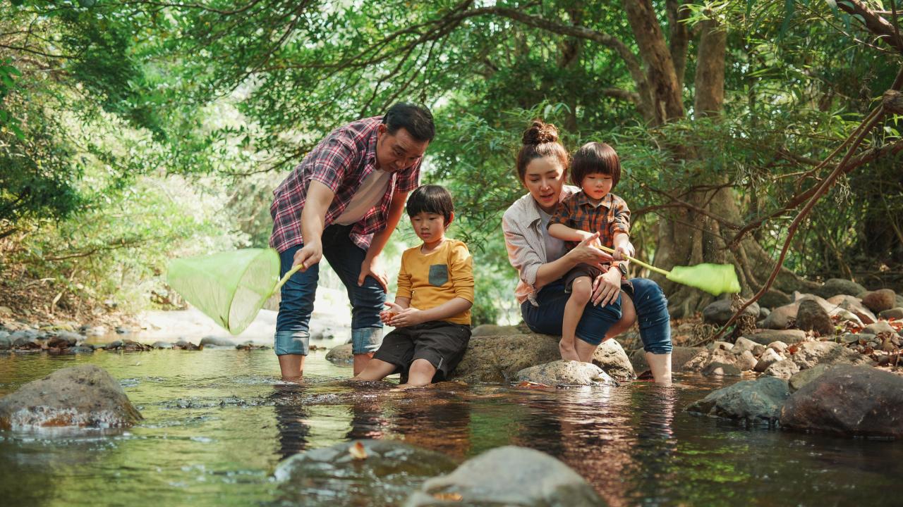 family fishes in river with green trees in background