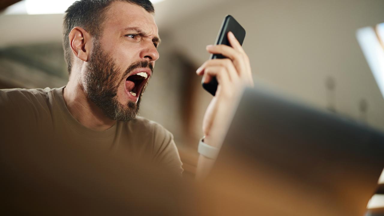 Man with beard seeming shocked by what he sees on cell phone