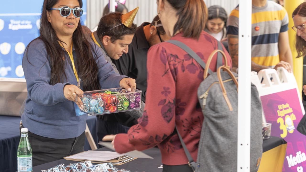 A customer makes a big purchase at the Arneson Egghead Collection Pop-Up Shop at the Manetti Shrem Museum. On the counter is a column of blue Egghead sunglasses.