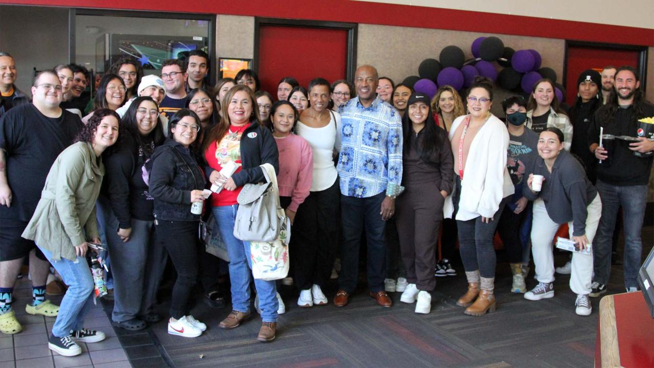 Group photo of students and Chancellor Gary S. May in movie theater lobby.