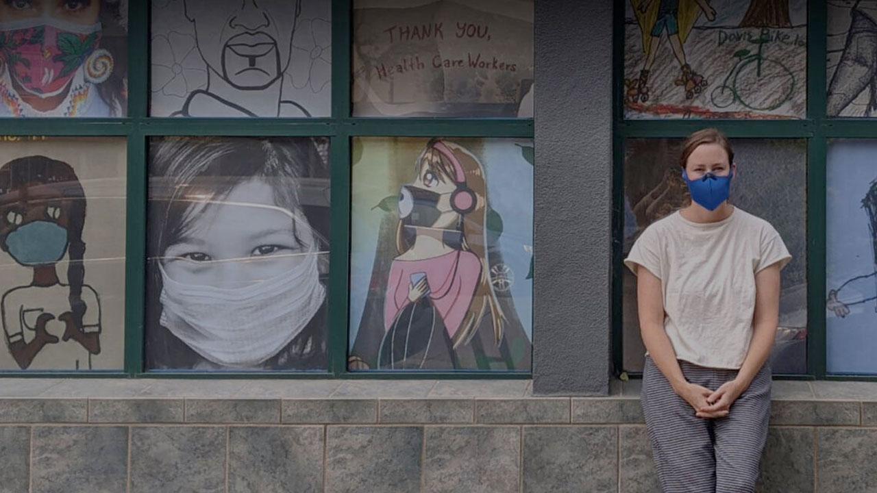 A masked woman stands in front of a mural in Davis, Ca
