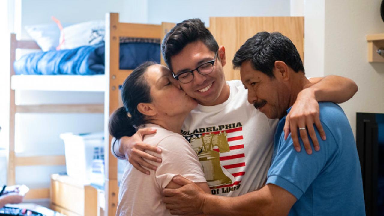 a student hugging his parents inside a residence hall room