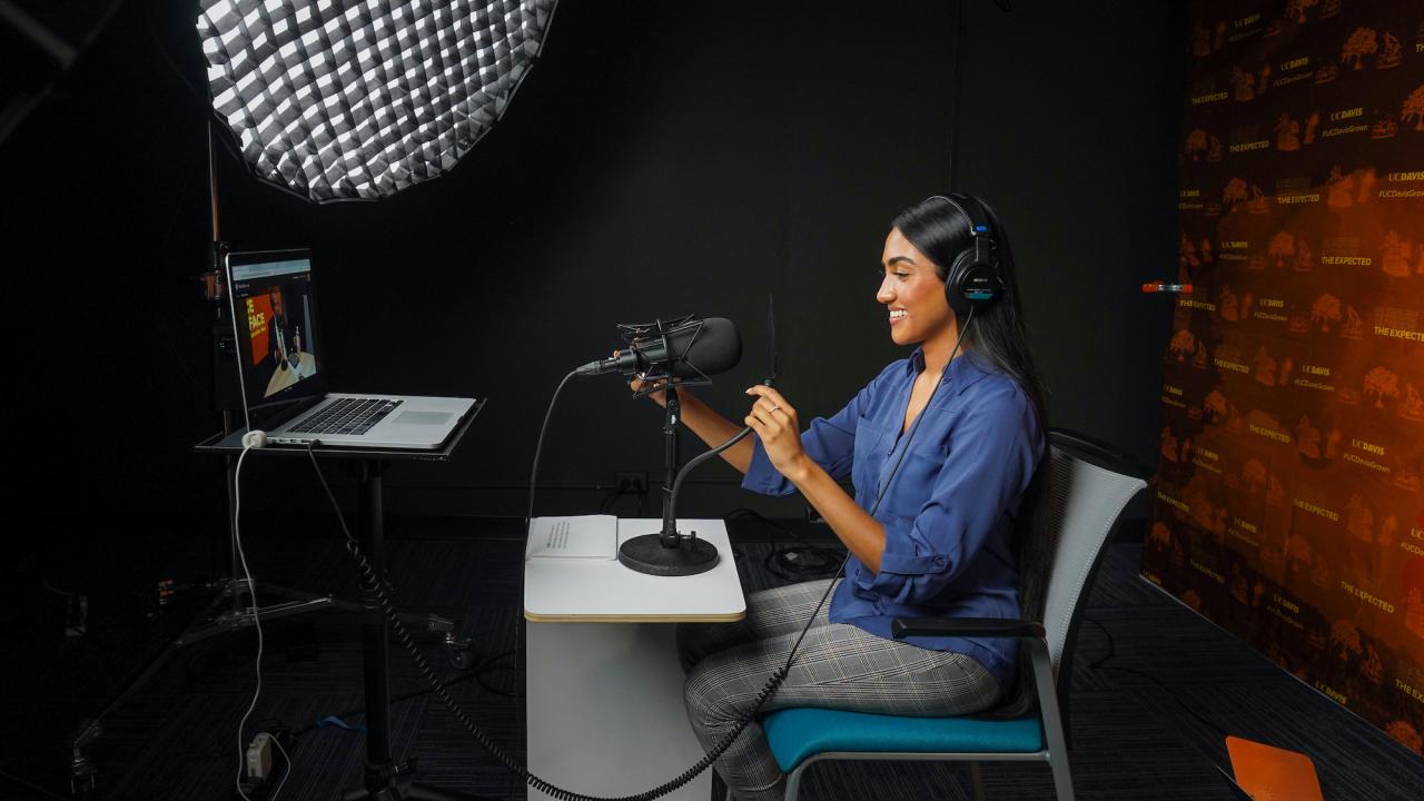 A student smiles in a podcast studio at UC Davis. 