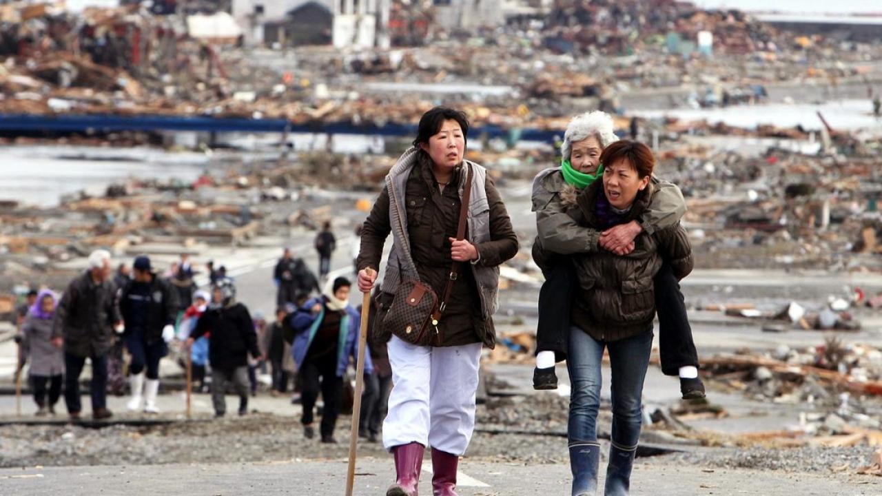 Women help each other leave the flattened city of Tohuku, Japan the day after a 9.0 earthquake on March 11, 2011 triggered a tsunami and nuclear meltdown, killing thousands.