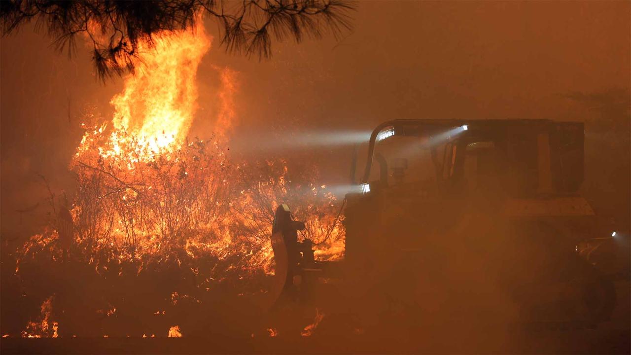 Firefighters and heavy equipment with fire in background