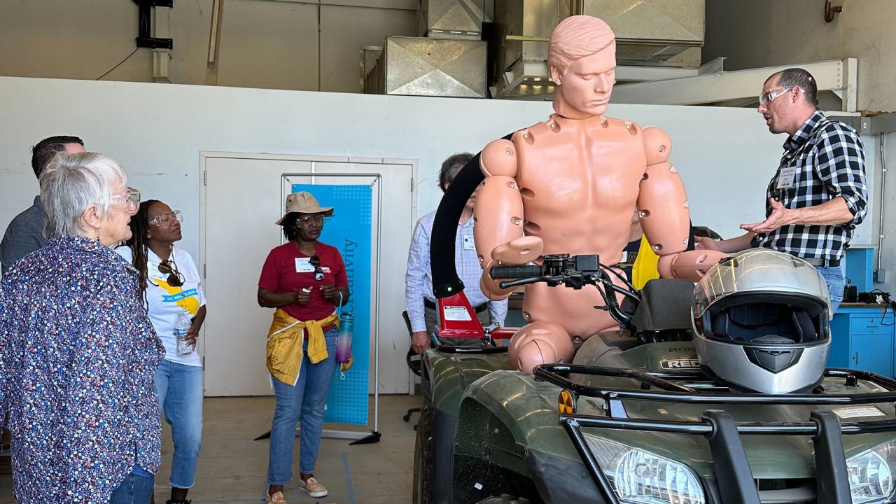 Tour group views all-terrain vehicle with mannequin in the driver's seat, for safety research