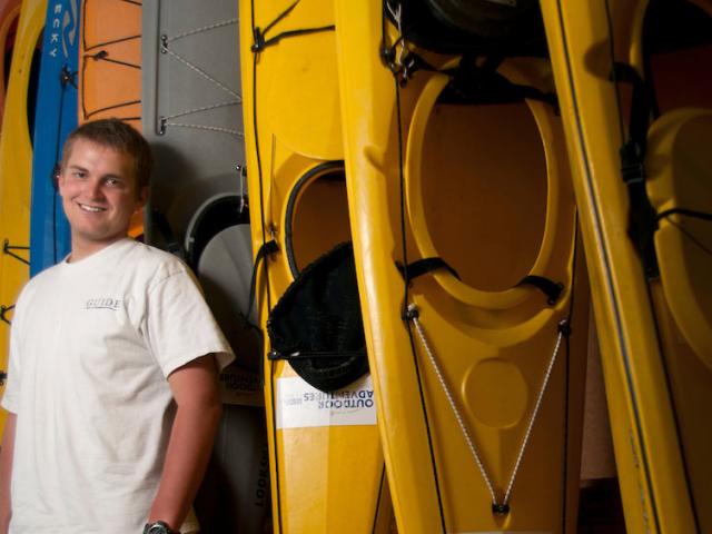 A male student stands in front of a stack of colorful kayaks