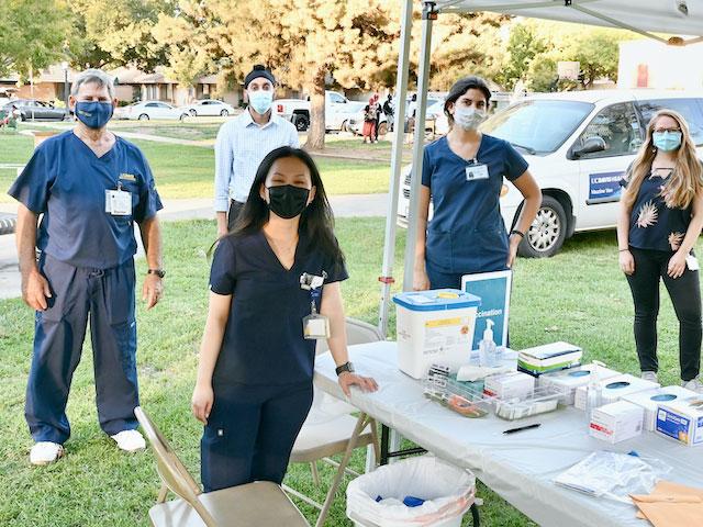 A group of doctors nurses poses under a vaccination tent on the UC Davis campus