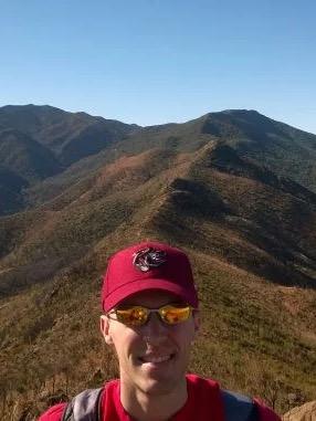 Atmospheric scientist Matt Igel in red ball cap, sunglasses and red shirt with mountain backdrop
