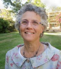 Head and shoulders of woman with grey curly hair and glasses photographed outdoors
