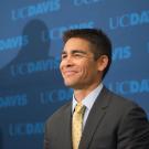 Intercollegiate Athletics Director Kevin Blue smiles in front of a UC Davis backdrop.