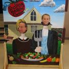 Man and boy stick their heads through a cut-out board with the American Gothic as the theme